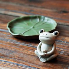 a frog figurine sitting on top of a wooden table next to a leaf