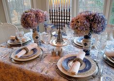 the table is set with blue and white plates, napkins, silverware, and purple flowers