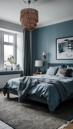 a bedroom with blue walls and grey bedding in front of a large window that has a painting on the wall