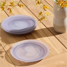 two white plates sitting on top of a wooden table next to a vase with yellow flowers