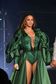 the singer is wearing a green outfit and revealing her cleavage in front of an audience