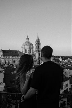 a man and woman standing on top of a building looking at the city below them