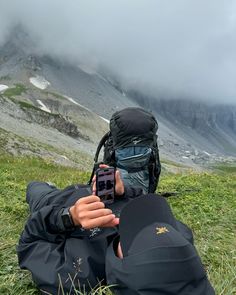 a man laying on top of a lush green field next to a mountain covered in clouds