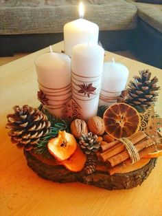 a table topped with candles and pine cones on top of a wooden slab filled with fruit