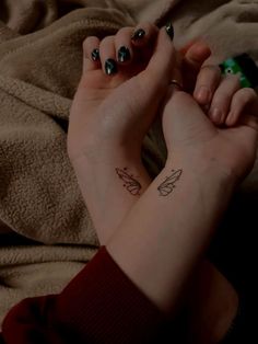 two hands holding each other with small tattoos on their wrists and wristbands,