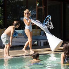 a woman and two children playing in a pool with a basketball net on the side