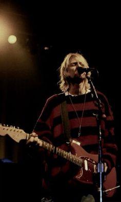 a man standing in front of a microphone while holding a guitar