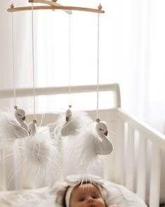 a baby laying in a crib with white feathers hanging from it's head