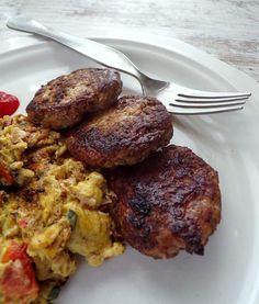 a plate with eggs, sausage and tomatoes on it next to a knife and fork