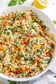 a white bowl filled with pasta salad next to lemon wedges