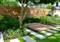 an outdoor garden with grass, trees and stepping stone steps leading up to a wooden fence