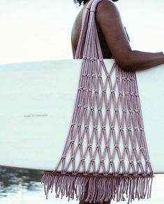 a woman carrying a white surfboard while standing next to the water with a pink bag on her shoulder