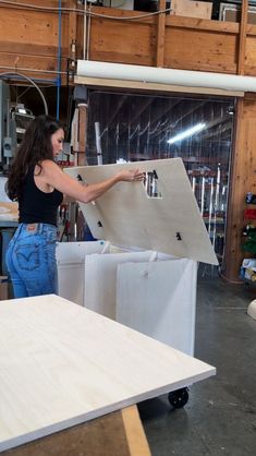 a woman is working on a piece of furniture in a shop or workshop with unfinished boards and plywood