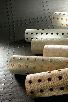 four rolls of fabric with holes on them sitting next to each other in front of a metal surface