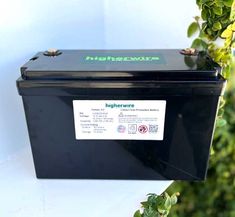 a black box sitting on top of a table next to some plants and trees in front of a white wall