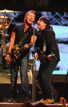 two men standing next to each other on stage with guitars in their hands and one holding a microphone