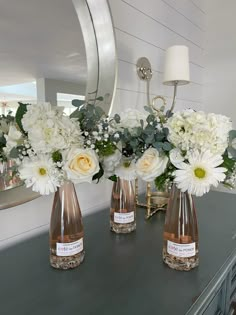 three vases filled with white flowers sitting on top of a table next to a mirror