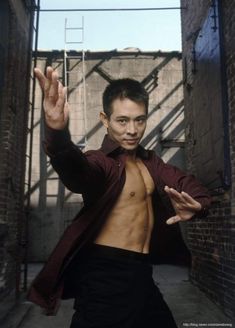 a man with no shirt standing in an alley way holding his hands up to the side