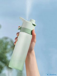 a hand holding a green and white water bottle with spouting from the top