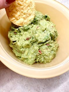 a person is dipping guacamole into a bowl with a tortilla chip