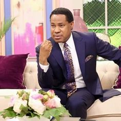 a man in a suit sitting on top of a couch next to a vase with flowers