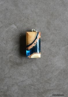 a square shaped pendant with blue and brown designs on it's side sitting on a gray surface