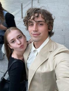 a young man and woman taking a selfie on the street in front of some people