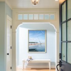 an entry way with a bench and a painting on the wall above it that says sailboat