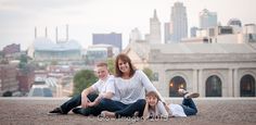 a woman and two children sitting on the ground in front of a cityscape