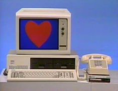 an old computer with a heart on the screen and two telephones next to it