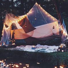 a tent is set up in the woods with lit candles around it and there are lights on the ground