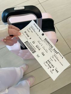 a person holding a ticket and sitting next to a pink suitcase