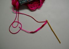 a ball of yarn and a knitting needle on a white surface with a pink thread