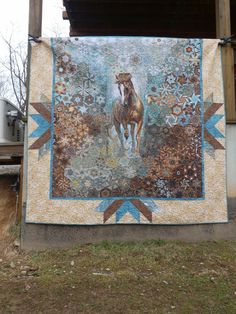 a quilt hanging from the side of a building with a horse on it's back