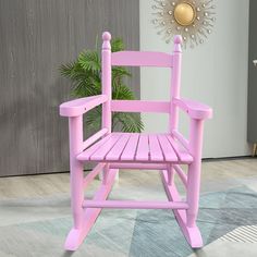 a pink rocking chair sitting on top of a rug next to a potted plant