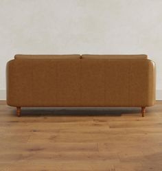 a brown couch sitting on top of a hard wood floor next to a white wall