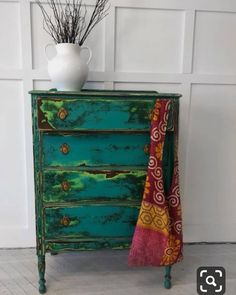 an old dresser painted in green and gold with flowers on top, next to a white vase