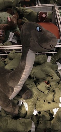 stuffed dinosaurs are piled up in a toy storage area, with one dinosaur looking at the camera