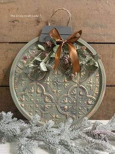 a christmas ornament hanging on a wall next to pine cones and evergreen branches