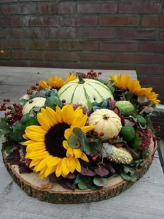 an arrangement of sunflowers and gourds on a wood slice for display