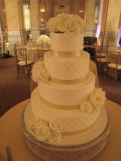 a wedding cake with white flowers on top is sitting on a table in a banquet room