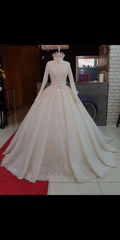 a white wedding dress on display in a room with a red carpet and brick wall