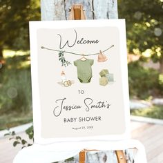 a welcome sign for a baby shower with clothes hanging from a line on a wooden easel