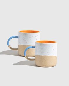 two white and orange coffee mugs sitting next to each other on a gray surface