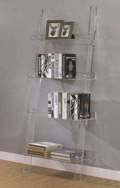 a clear shelf with books on it in front of a gray wall and wooden floor