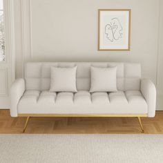 a white couch sitting on top of a hard wood floor next to a framed painting