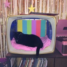 a black cat laying on top of a bed in front of an old tv set