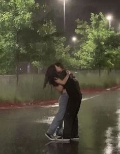 two people kissing on a skateboard in the rain at night with street lights behind them