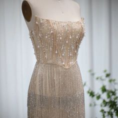 a dress on display in front of a white wall with flowers and greenery behind the mannequin