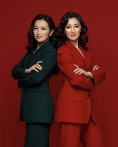 two women standing next to each other in front of a red background with their arms crossed